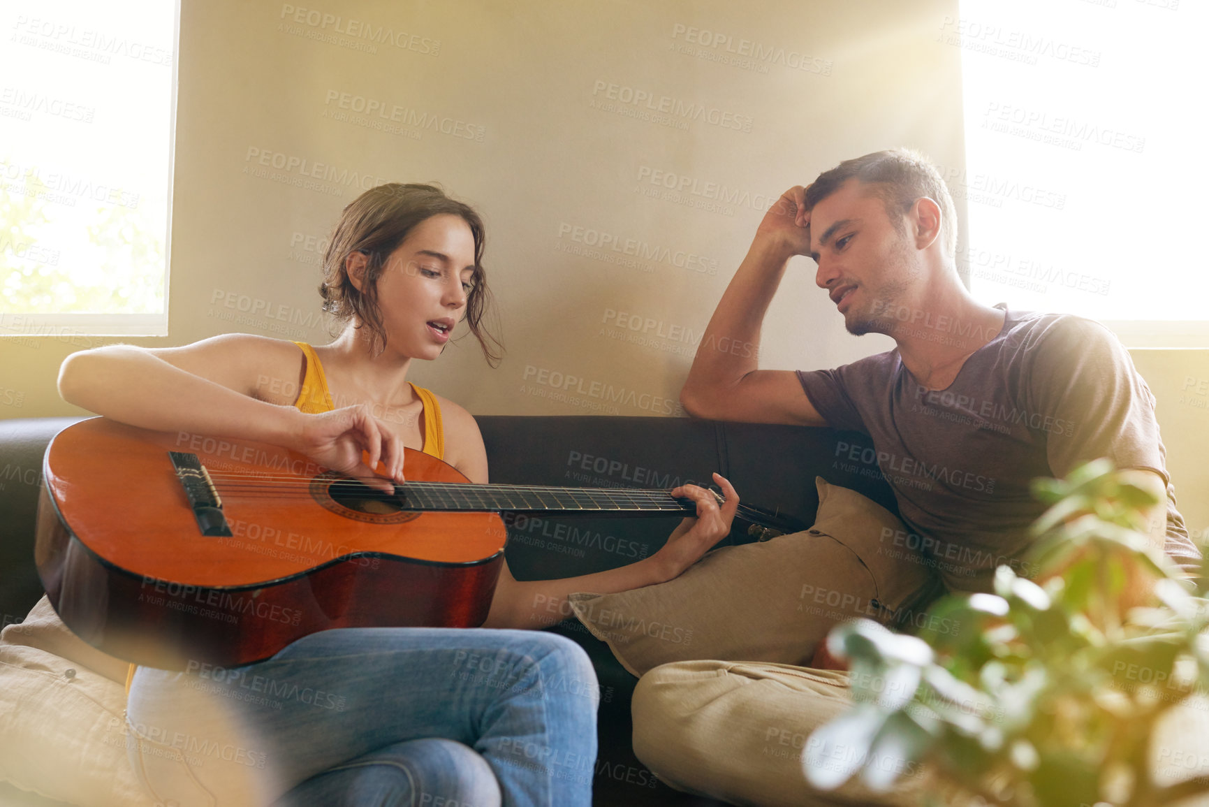 Buy stock photo Shot of a young woman playing the guitar while relaxing on the sofa with her husband
