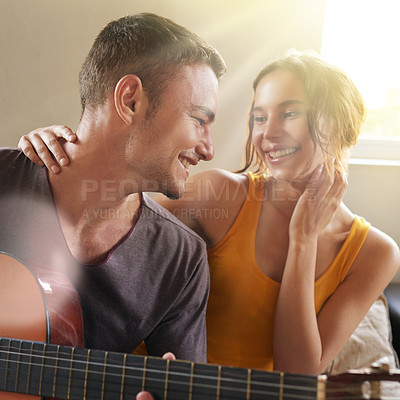 Buy stock photo Shot of a young man playing the guitar while relaxing on the sofa with his wife