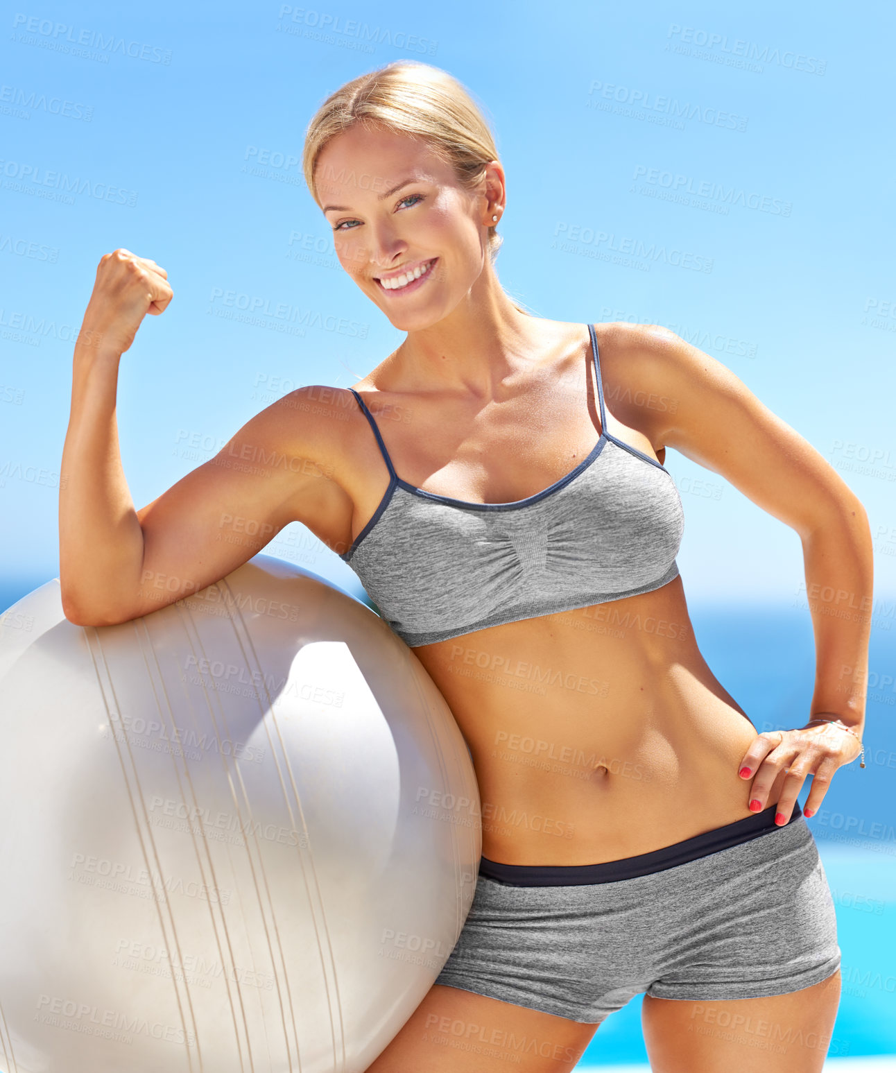 Buy stock photo Portrait of an attractive young woman flexing her bicep on an exercise ball