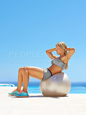 Buy stock photo Shot of an attractive young woman working out with an exercise ball by a swimming pool
