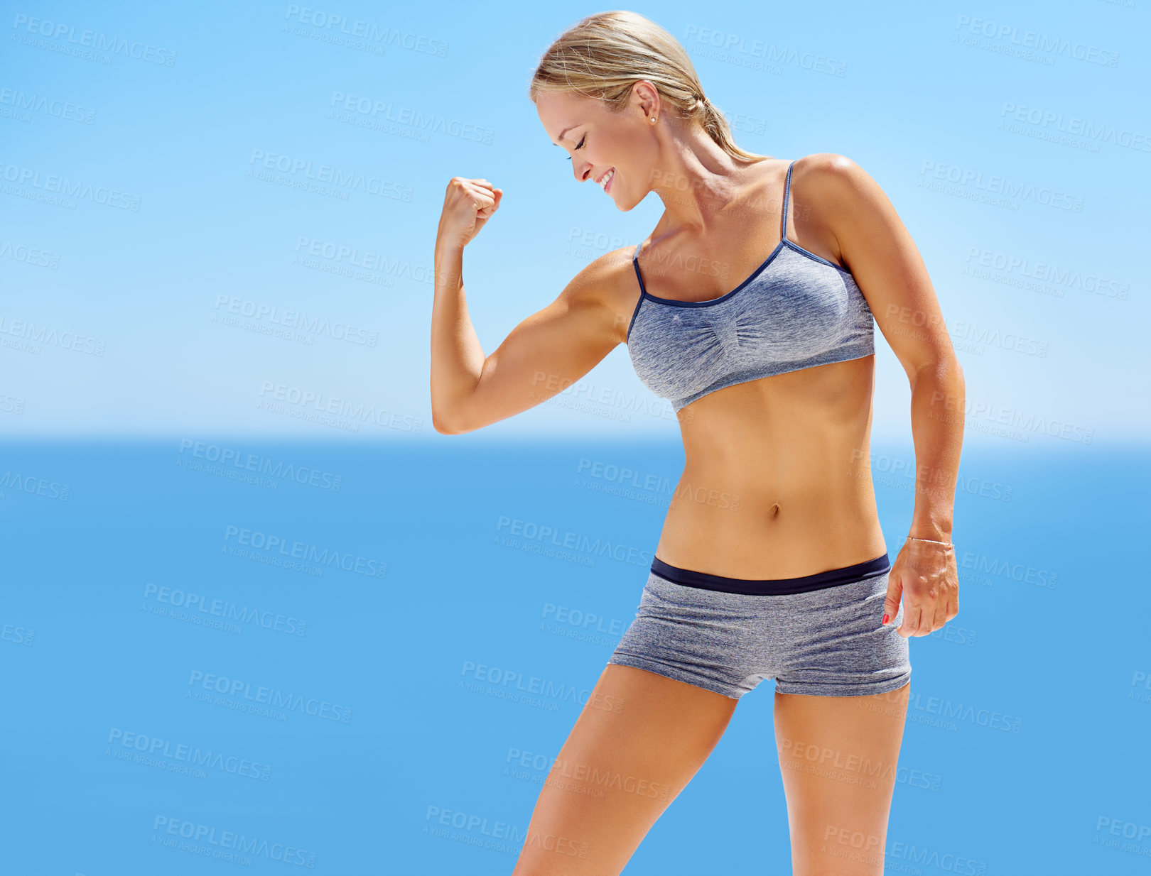 Buy stock photo Shot of an attractive young woman in exercise clothing flexing her bicep outside
