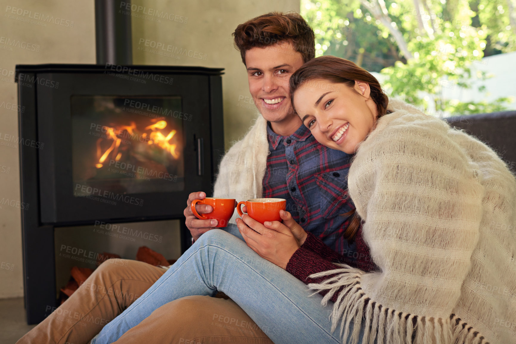 Buy stock photo Shot of a young couple drinking hot chocolate by the fireplace