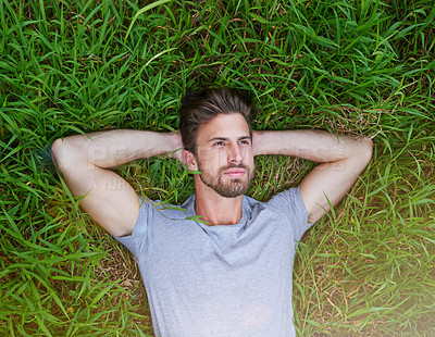 Buy stock photo High angle shot of a young man lying down on the grass with his hands behind his head
