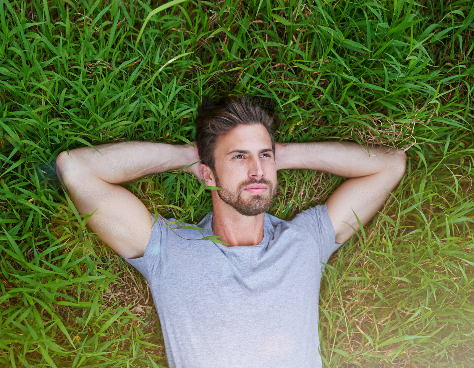 Buy stock photo High angle shot of a young man lying down on the grass with his hands behind his head