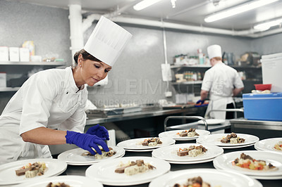 Buy stock photo Shot of a chef plating food for a meal service in a professional kitchen