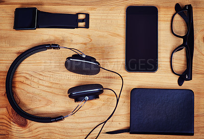 Buy stock photo Shot of headphones, a notebook, glasses and a smartphone and smart watch on a table