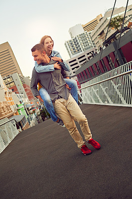 Buy stock photo Shot of a happy young couple enjoying a piggyback ride in the city