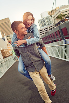 Buy stock photo Shot of a happy young couple enjoying a piggyback ride in the city