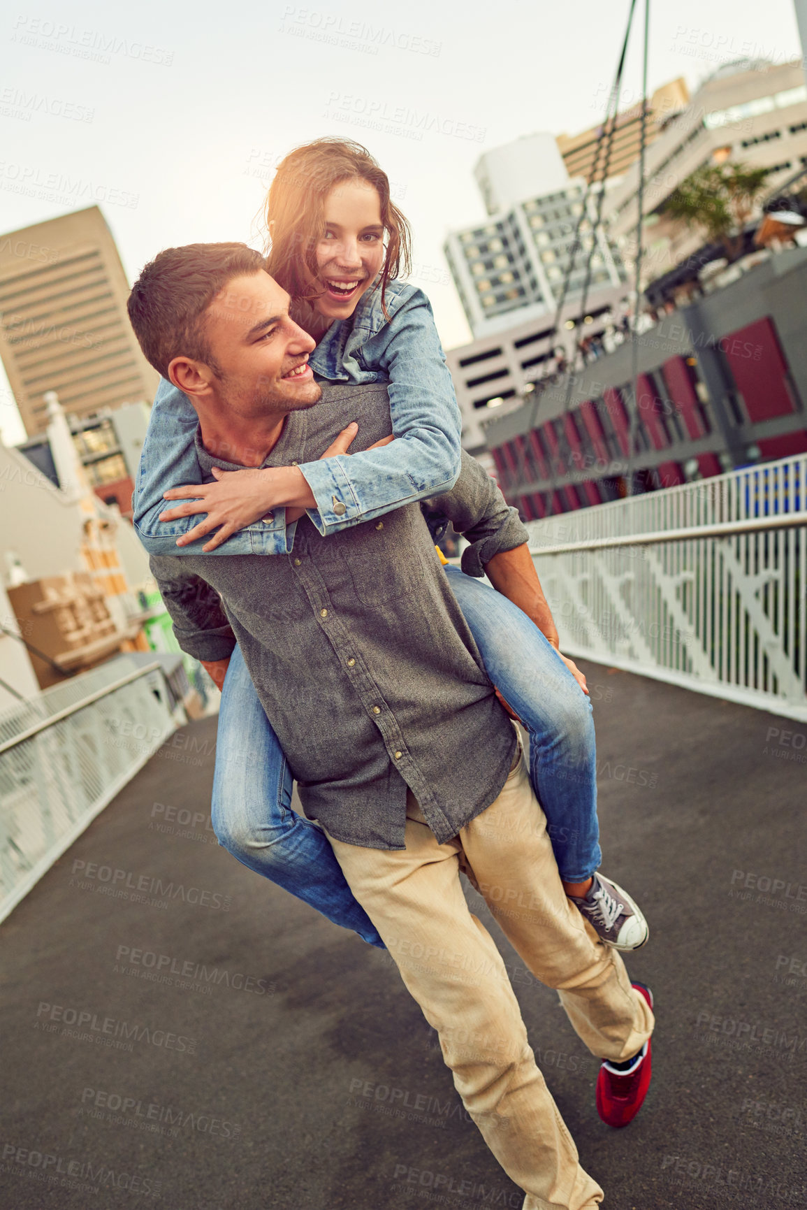 Buy stock photo Shot of a happy young couple enjoying a piggyback ride in the city