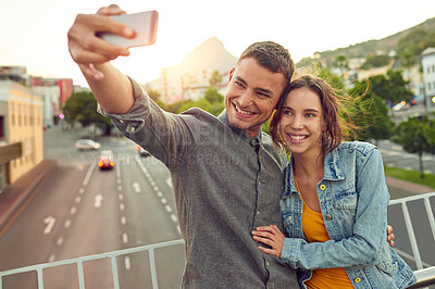 Buy stock photo Shot of a happy young couple taking a selfie together in the city