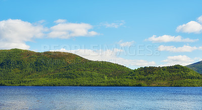 Buy stock photo Green hills by the seaside with a blue sky in Norway. Wild vibrant landscape in Nordland. A calm sea near an uninhabited island wilderness against a bright cloudy horizon. Peaceful nature scene