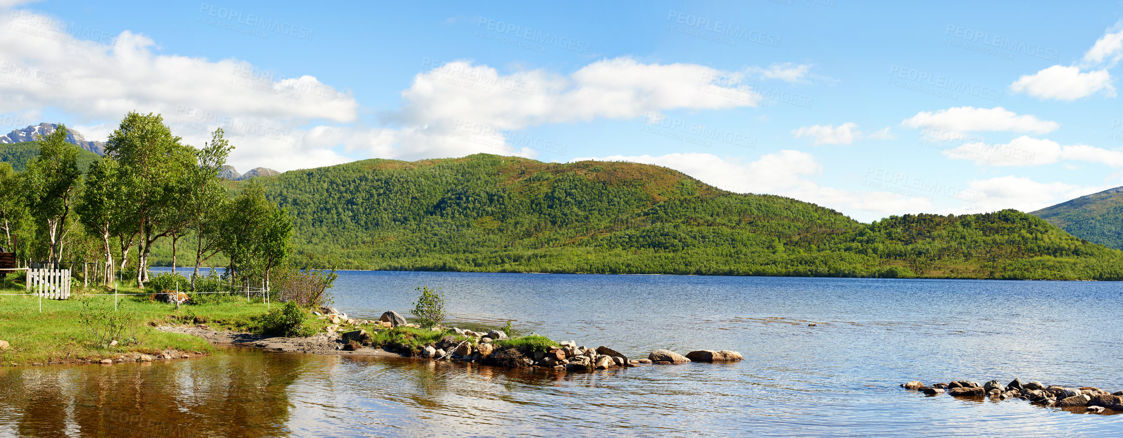 Buy stock photo Landscape of a lake with trees, green grass hills. A scenic waterhole surrounded by an empty forest land. Coast of the mountain lake with blue cloudy sky in Nordland near Bodo, Norway