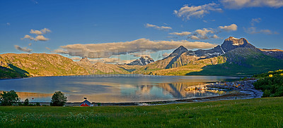 Buy stock photo Countryside landscape in Nordland, Bodo, Norway with
glistening waters on a lake near a majestic mountainscape during sunset. Blue sky  with lush green grass and a little house on a river bank
