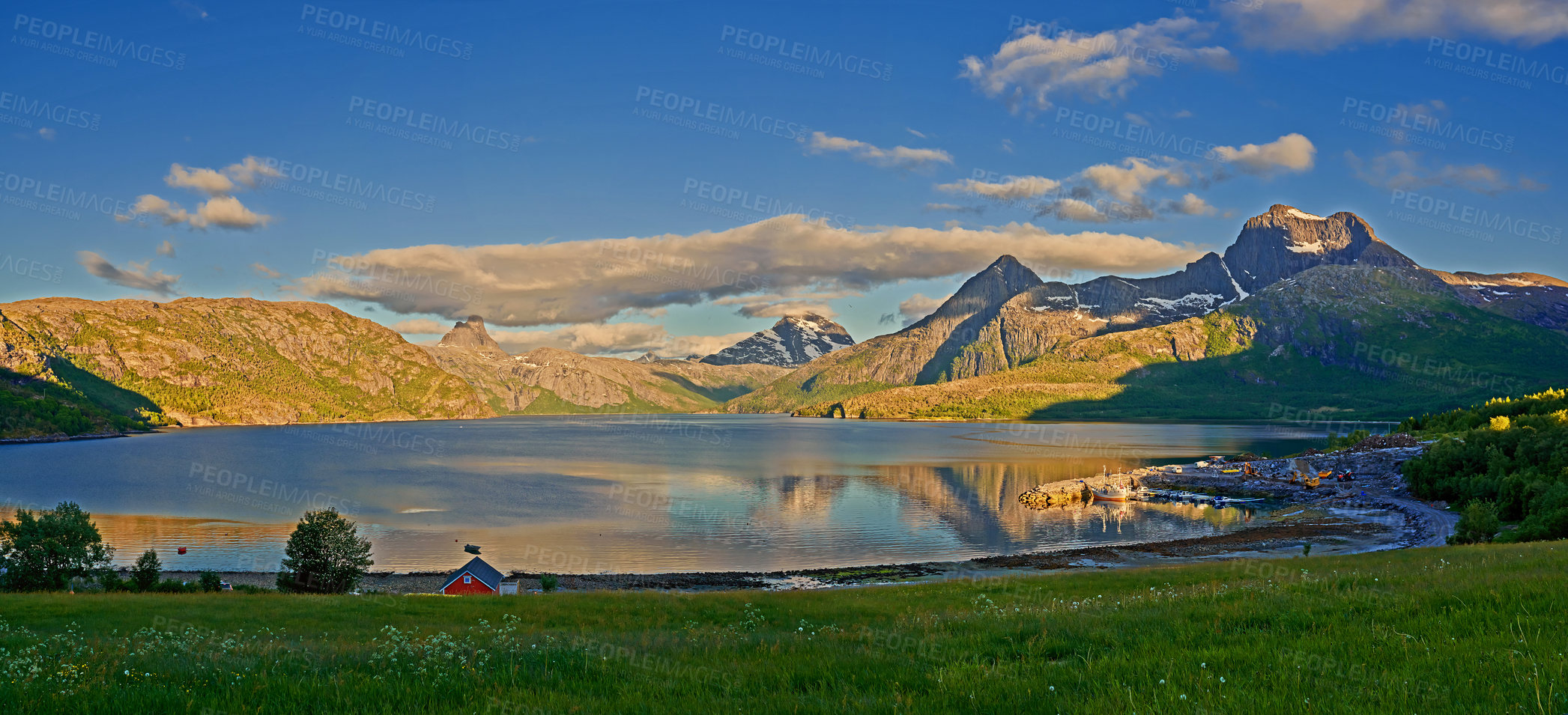 Buy stock photo Countryside landscape in Nordland, Bodo, Norway with
glistening waters on a lake near a majestic mountainscape during sunset. Blue sky  with lush green grass and a little house on a river bank
