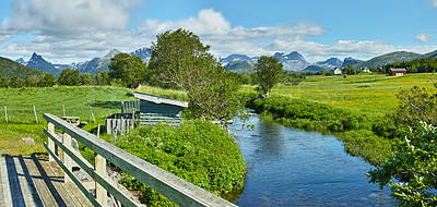 Buy stock photo Landscape of a river between hills and mountains. Green foliage by the riverbank with a blue sky in Norway. Calm water near a vibrant wilderness against a bright cloudy horizon. Peaceful nature scene