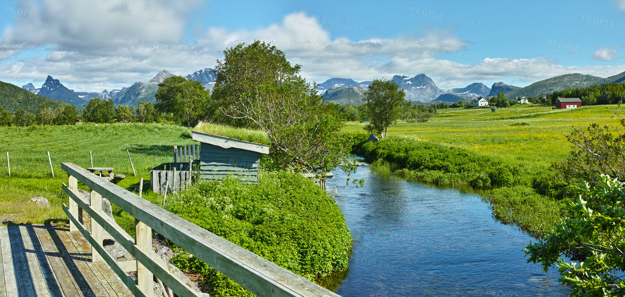 Buy stock photo Landscape of a river between hills and mountains. Green foliage by the riverbank with a blue sky in Norway. Calm water near a vibrant wilderness against a bright cloudy horizon. Peaceful nature scene