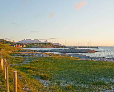 Buy stock photo Green hills by the seaside with a blue sky in Norway. Wild vibrant landscape in Nordland. A calm sea near an uninhabited island wilderness against a warm dark cloudy horizon. A peaceful nature scene