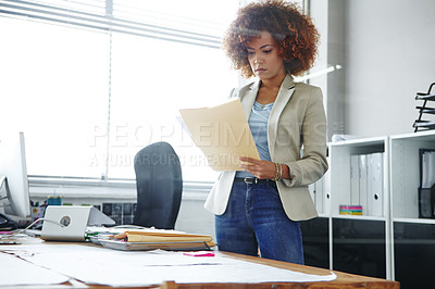 Buy stock photo Cropped shot of a beautiful young businesswoman looking over some documents in her office