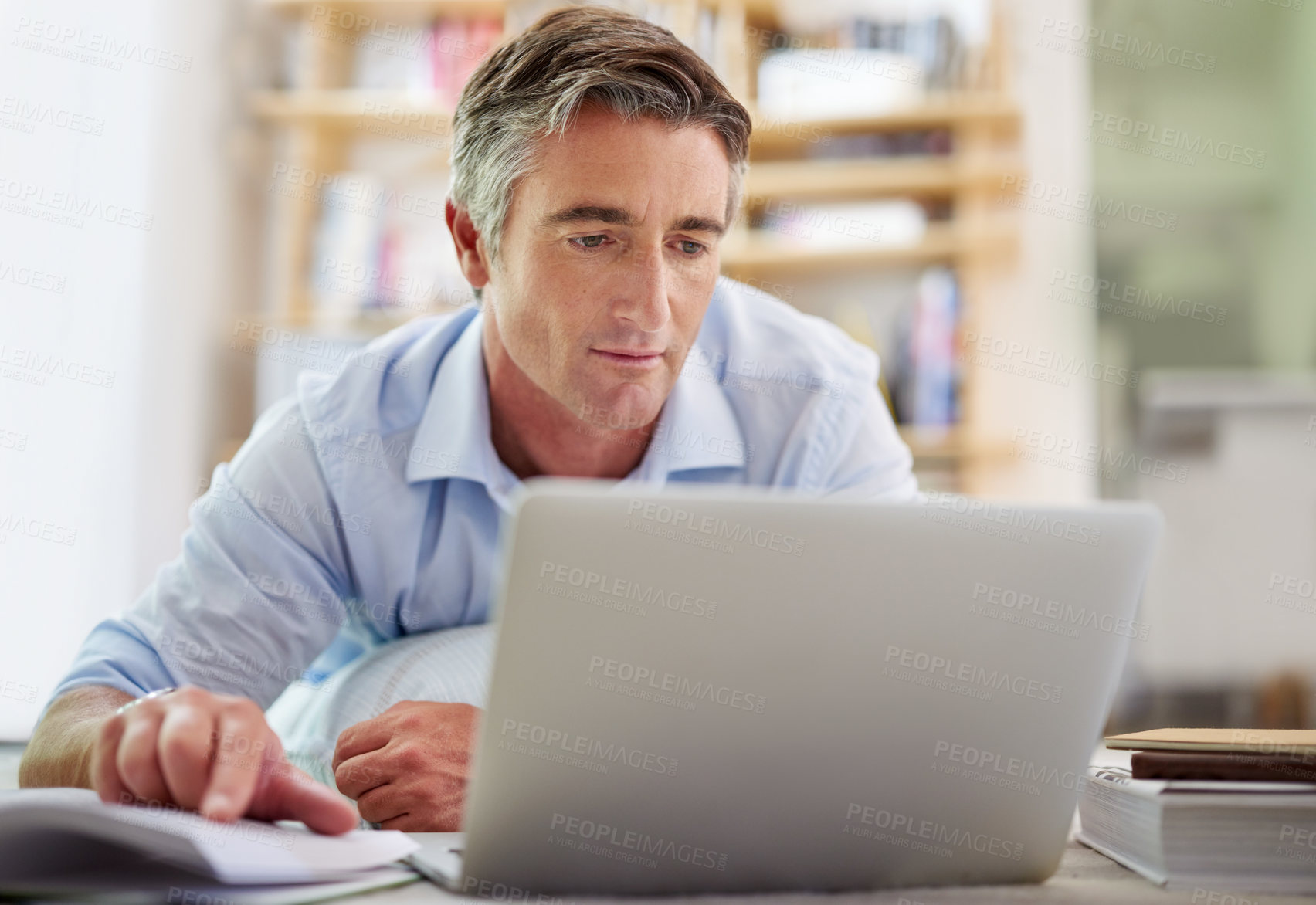 Buy stock photo Shot of a handsome mature man lying on his living room floor using a laptop