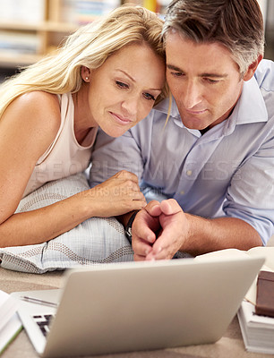 Buy stock photo Shot of a mature couple lying on their living room floor with a laptop and book