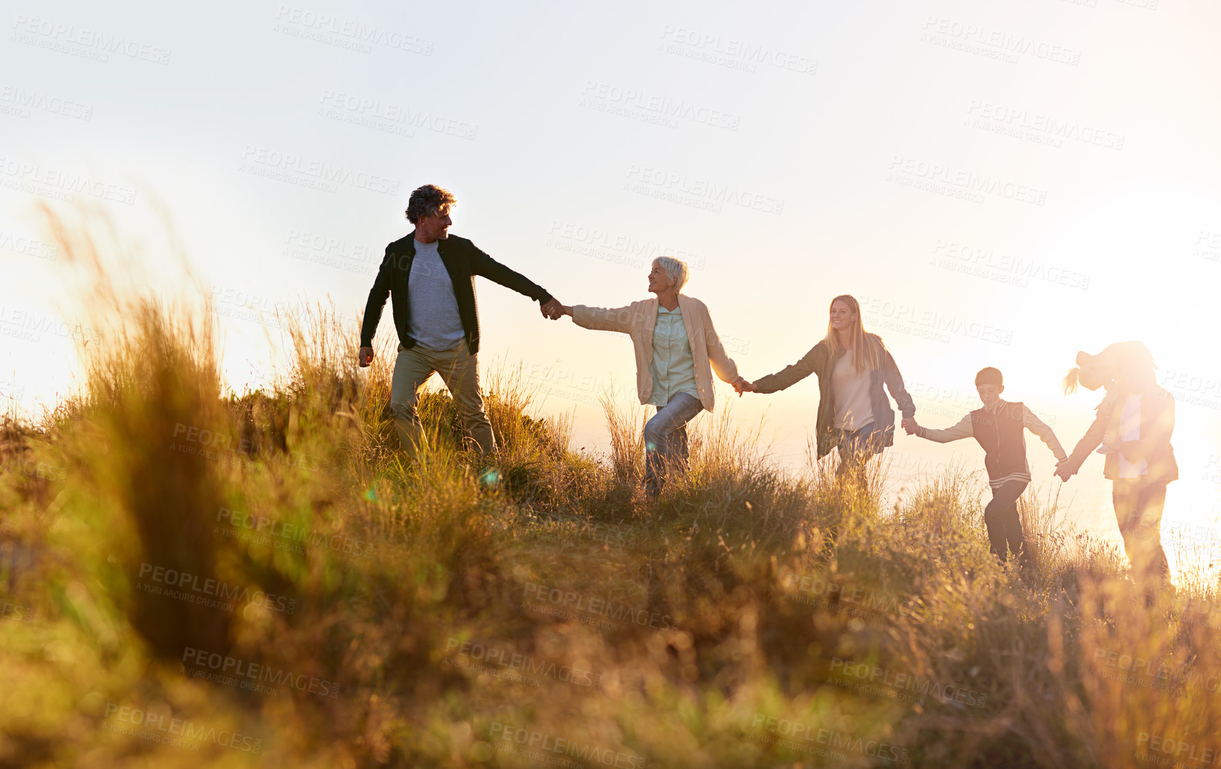 Buy stock photo Shot of a multi-generational family walking hand in hand across a field at sunset