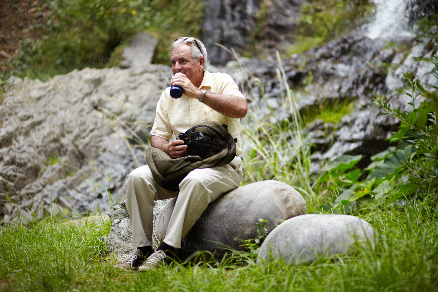 Buy stock photo Senior, man and drinking water in forest for break, sightseeing or vacation with waterfall and scenery. Elderly person in woods or nature to rest on holiday, adventure or experience with backpack