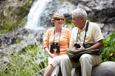 Buy stock photo Senior, man and woman with binocular for travel, sightseeing or holiday with happiness on rocks. Elderly, couple and face with smile for waterfall, vacation and adventure on retirement or tourism