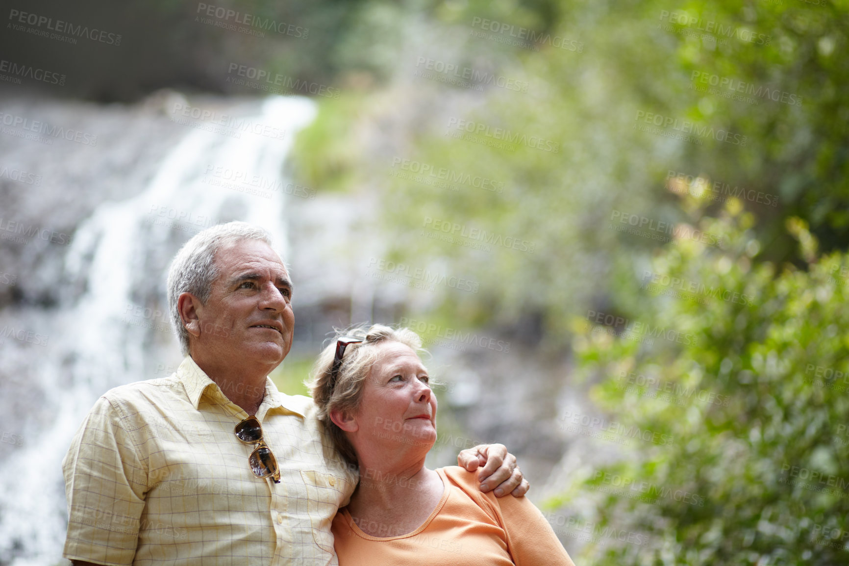 Buy stock photo An affectionate senior couple standing against the backdrop of a picturesque waterfall