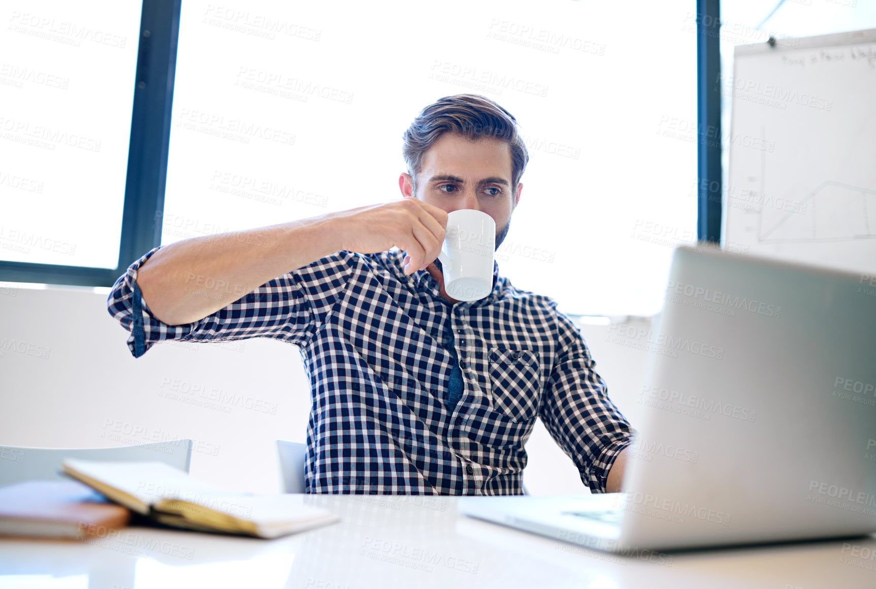 Buy stock photo Cropped shot of a handsome businessman drinking coffee while working on his laptop