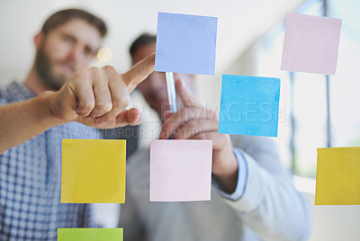 Buy stock photo Through the glass shot of two male coworkers arranging sticky notes on a wall during a meeting