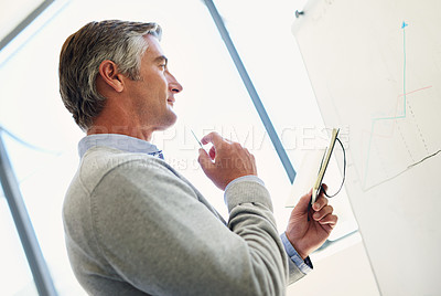 Buy stock photo A mature business looking thoughtful while standing at a whiteboard holding a notebook