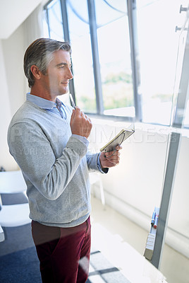 Buy stock photo A mature business looking thoughtful while standing at a whiteboard holding a notebook