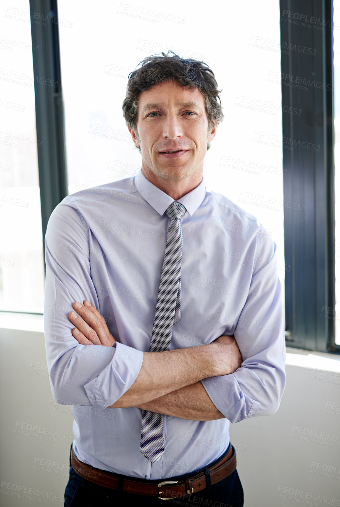 Buy stock photo Portrait of a businessman standing with his arms crossed by his office window