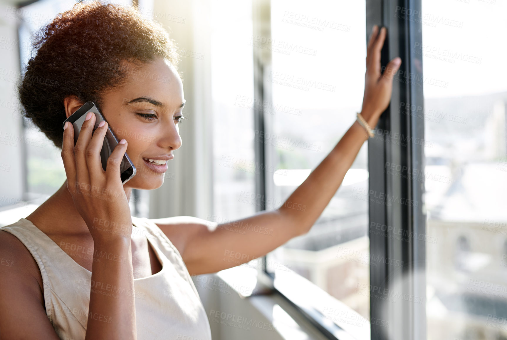 Buy stock photo A young businesswoman talking on her cellphone while standing by her office window