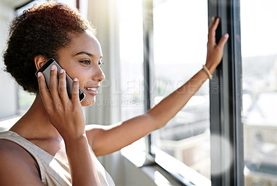 Buy stock photo A young businesswoman talking on her cellphone while standing by her office window