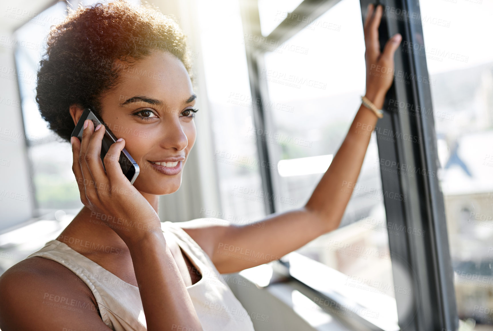 Buy stock photo A young businesswoman talking on her cellphone while standing by her office window