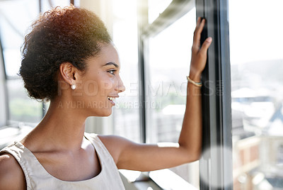 Buy stock photo Shot of an ambitious young businesswoman looking through her office window