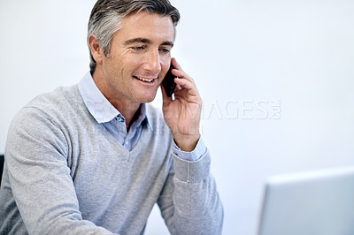 Buy stock photo Shot of a mature businessman talking on his cellphone while working at his laptop