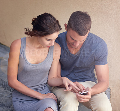 Buy stock photo Cropped shot of a young couple using a cellphone while sitting outside