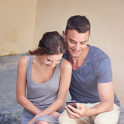 Buy stock photo Cropped shot of a young couple using a cellphone while sitting outside