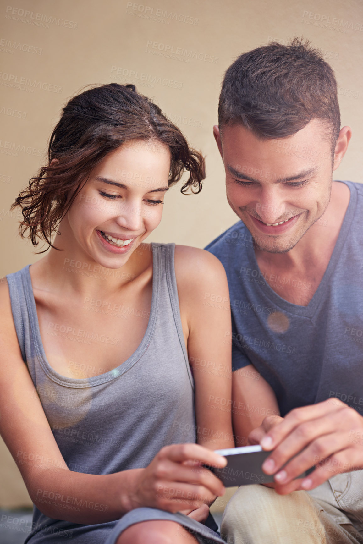 Buy stock photo Cropped shot of a young couple using a cellphone while sitting outside