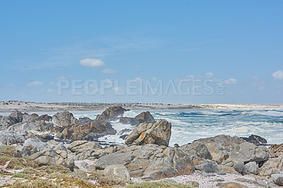 Buy stock photo A shallow rocky coastline in the Cape Province, South Africa. Ocean waves crashing on coastal rocks and boulders on a sunny summer day, blue clear skies, and a scenic tropical landscape beachfront