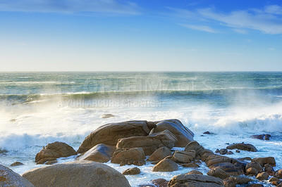 Buy stock photo Waves crashing onto a rocky shore. A seascape view of the ocean with blue sky copy space in Camps Bay, Cape Town, South Africa. Calm, serene and tranquil beach with relaxing scenery in nature