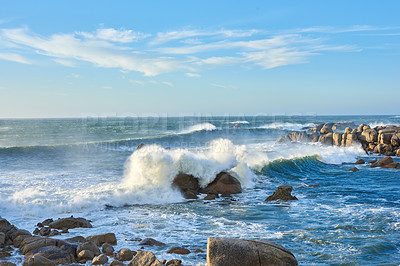 Buy stock photo A rocky coastline in the Cape Province, South Africa. Ocean waves crashing on coastal rocks on a sunny summer day with blue clear skies and a scenic tropical landscape beachfront in the Western Cape
