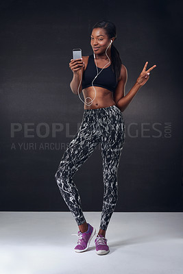 Buy stock photo Studio shot of a beautiful young woman using her phone during a workout against a black background