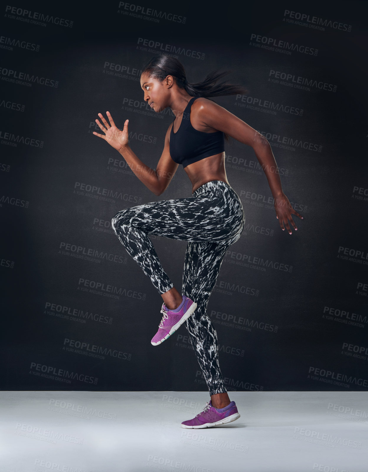 Buy stock photo Studio shot of a beautiful young woman jogging on the spot against a black background