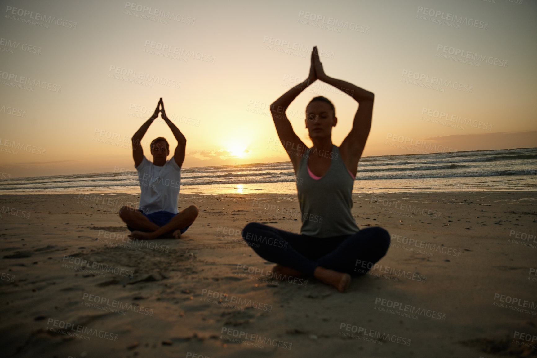 Buy stock photo Shot of a couple doing yoga on the beach at sunset