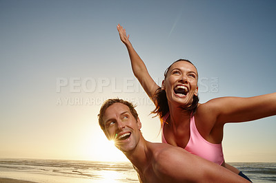 Buy stock photo Shot of a man giving his girlfriend a piggyback ride at the beach