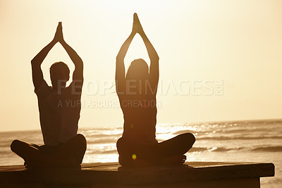 Buy stock photo Shot of a couple doing yoga by the sea at sunset