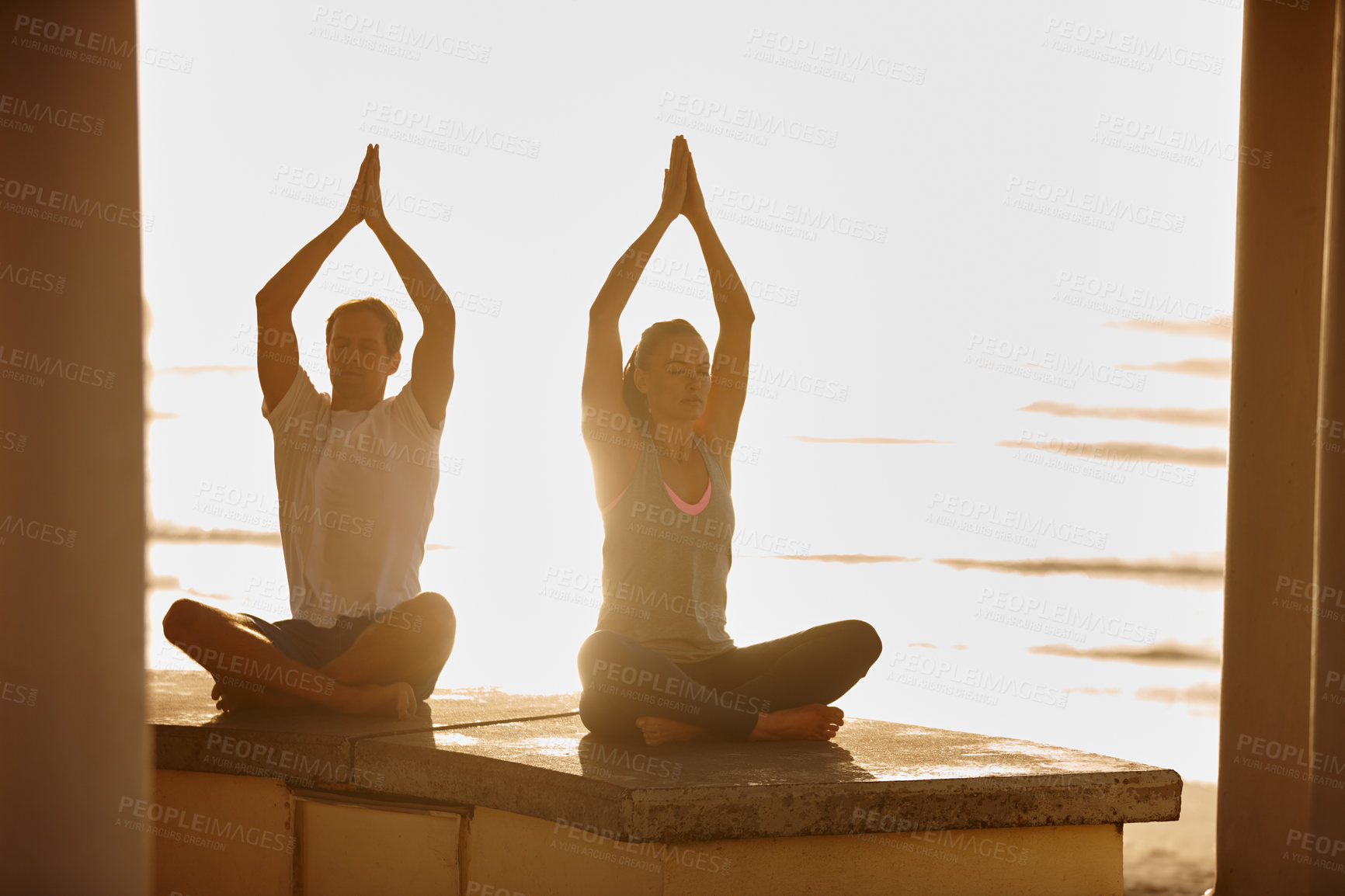 Buy stock photo Shot of a couple doing yoga by the sea at sunset